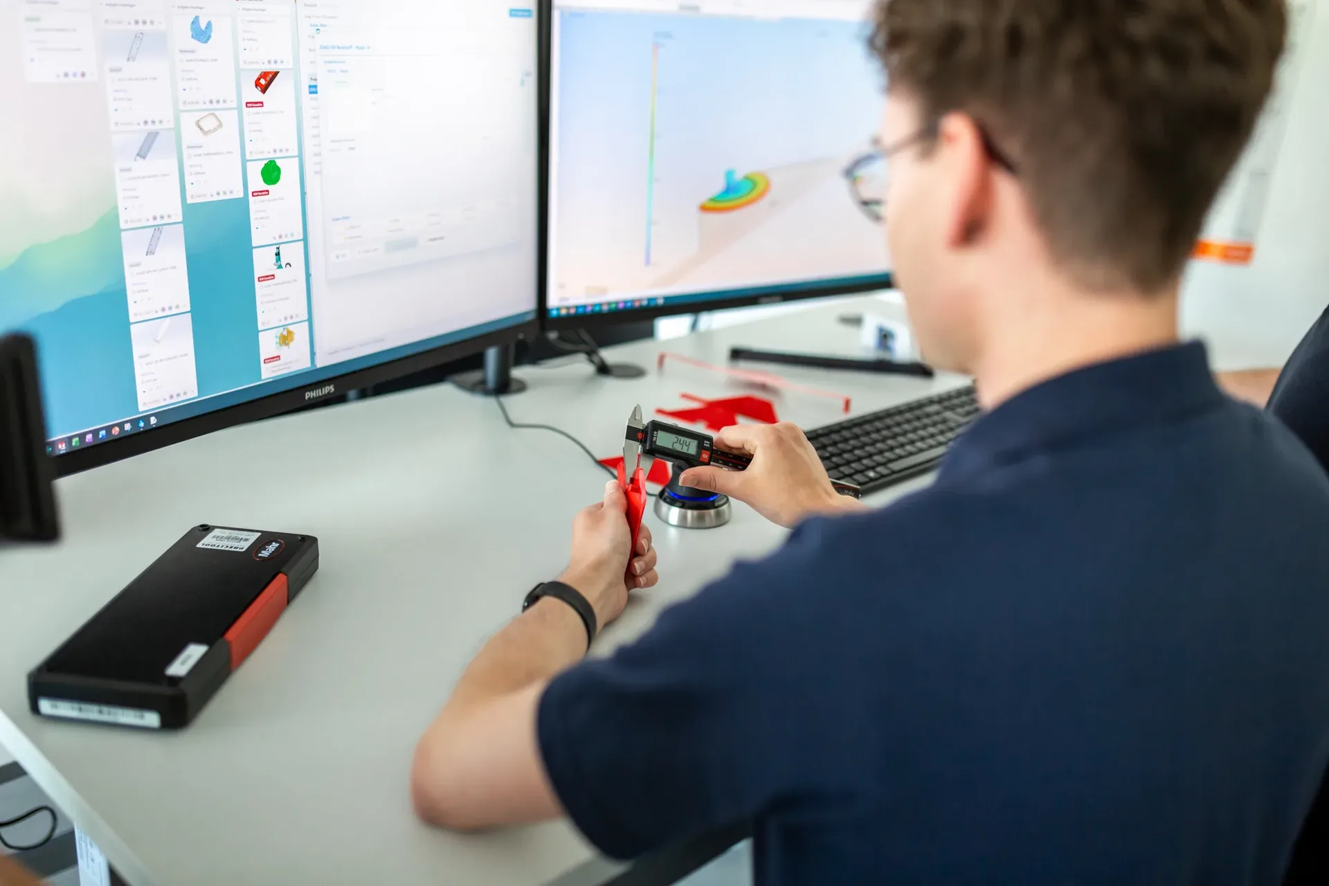 Ingenieur prüft ein Bauteil per Messschieber gegen die CAD-Konstruktion am Bildschirm